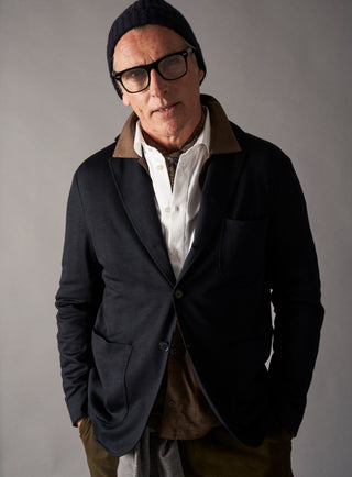 Man wearing a dark coat, white shirt, and glasses against a gray background