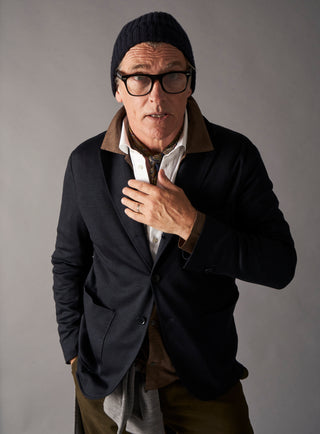 Man wearing a dark coat, beanie, and glasses against a gray background